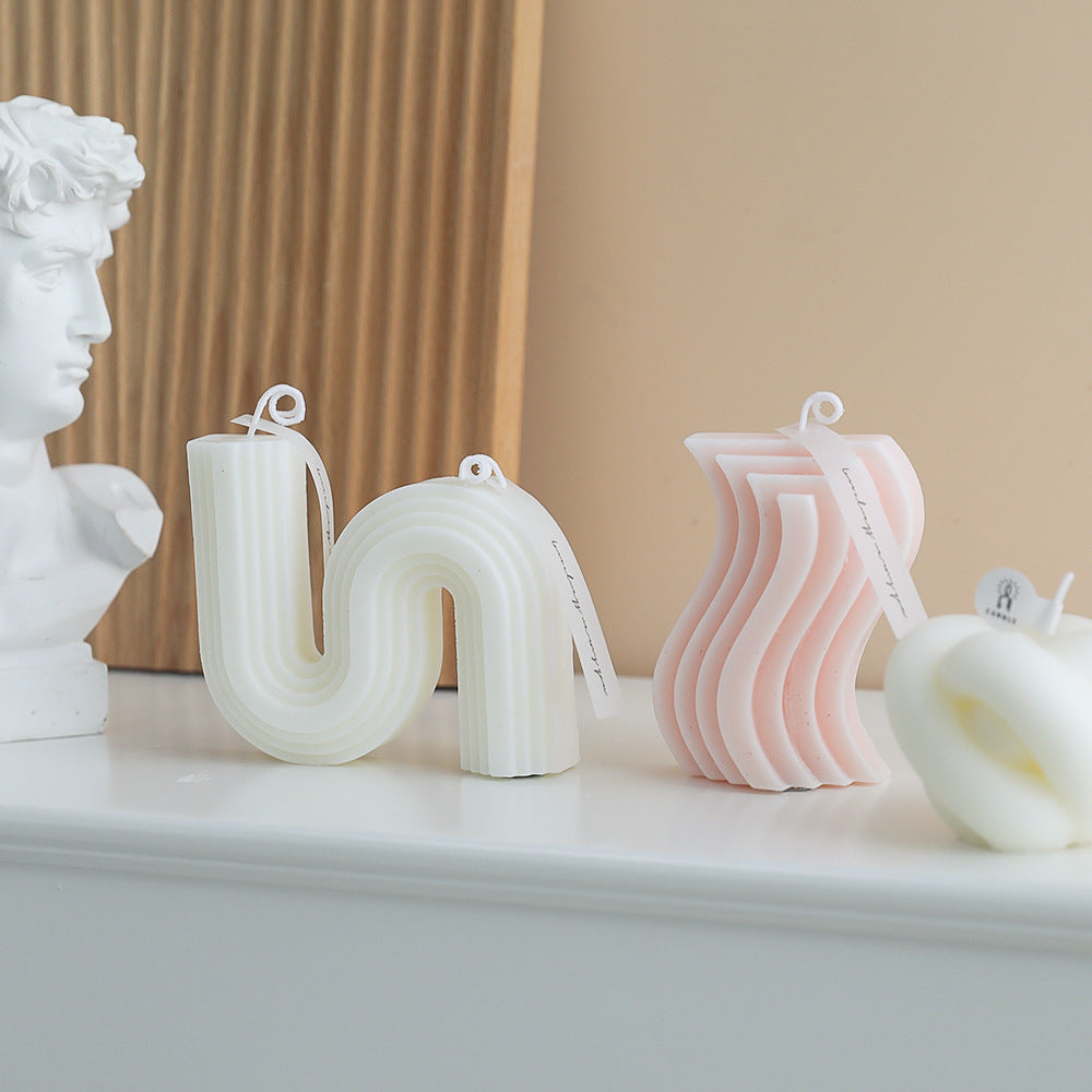 Decorative candles shaped like letters on a shelf with a classical bust in the background.