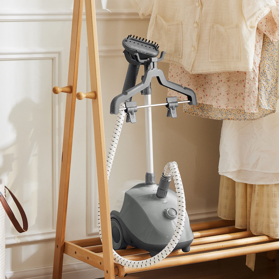 Gray handheld steamer on a wooden stand with clothes in the background