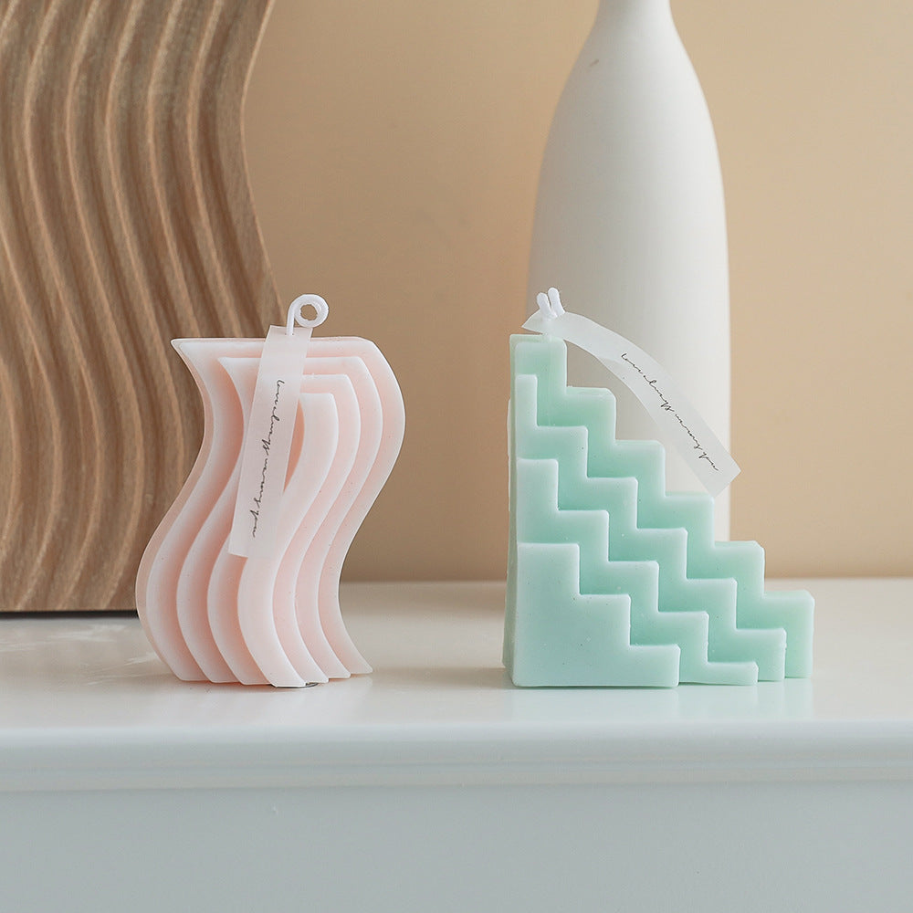 Two geometrically shaped candles, one pink and one green, on a neutral background.